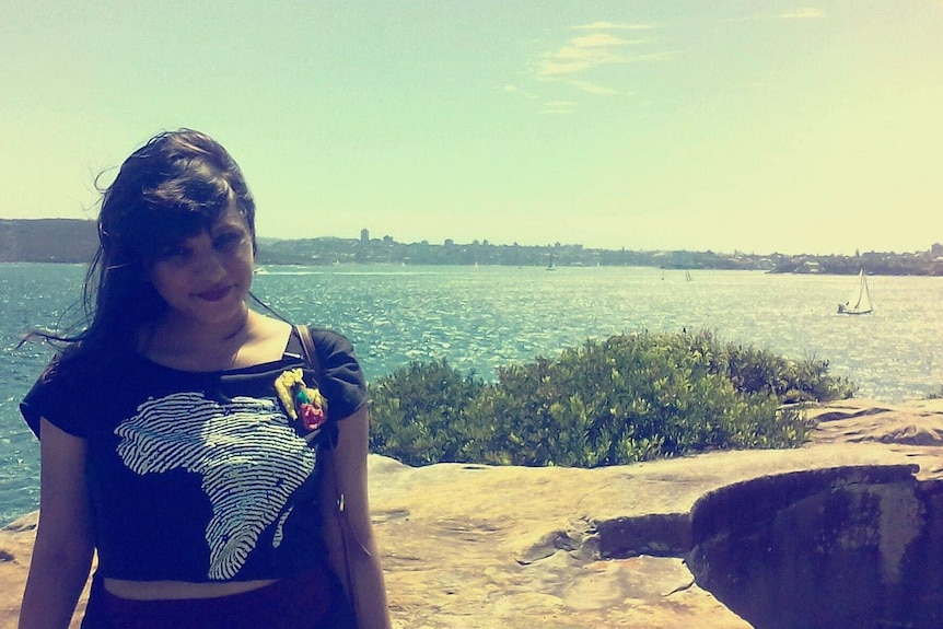 A young, dark-haired woman standing at the beach.