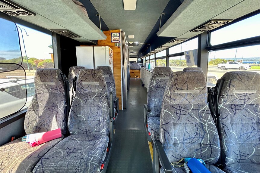 The inside of a large bus with seats at the front and a kitchen and beds in the back. 