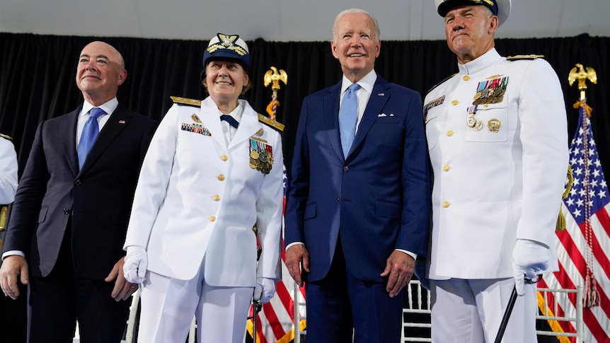 Two men in suits pose with a woman and a man wearing all-white uniforms and blue and white caps.