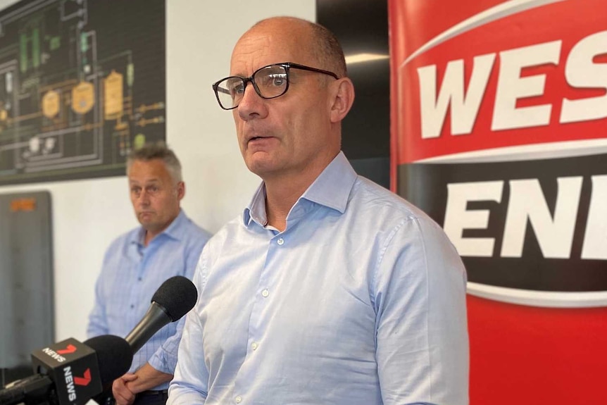 A bald man with glasses standing in front of microphones and a West End sign