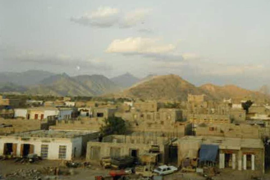 Houses and dilapidated cars sit in front of mountains in Yemen, outside the Al Gahain refugee camp