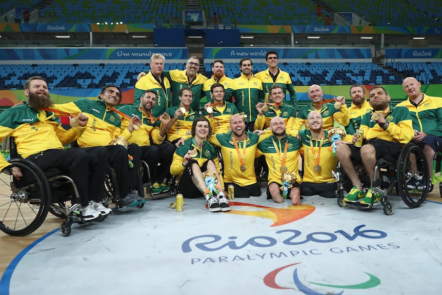 Australia's Paralympic wheelchair rugby team sit in their chairs and on the court for a group shot with their gold medals.