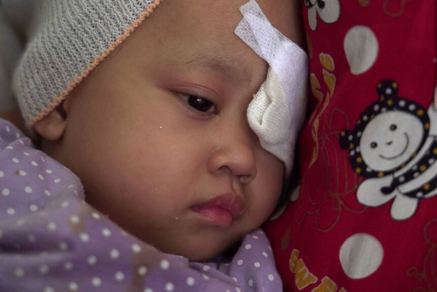 Raihana Fitri cuddles up to her mum as a bandage covers her left eye.
