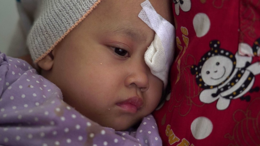 Raihana Fitri cuddles up to her mum as a bandage covers her left eye.