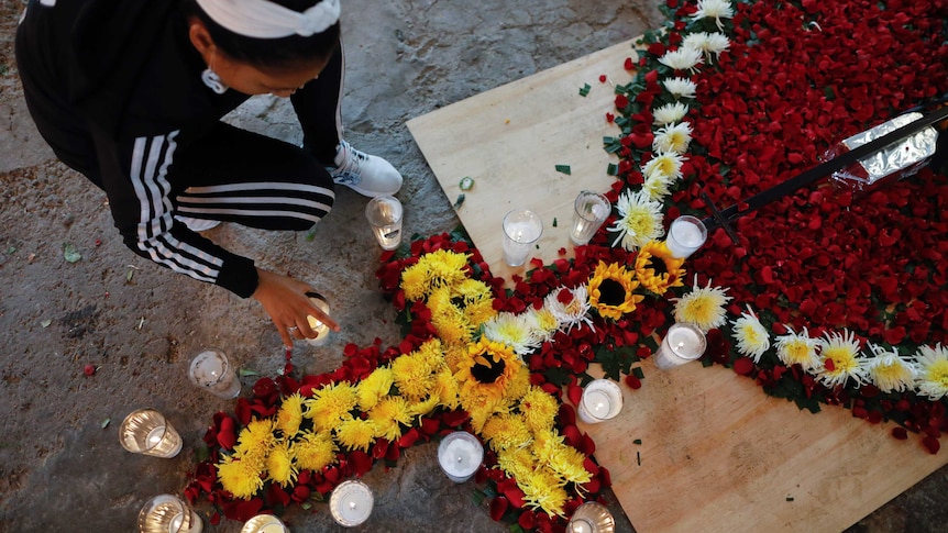 A woman places candles around red, white and yellow flowers arranged in the form of a catholic form of a catholic rosary.