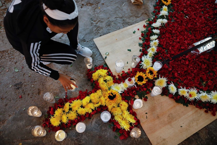 A woman places candles around red, white and yellow flowers arranged in the form of a catholic form of a catholic rosary.