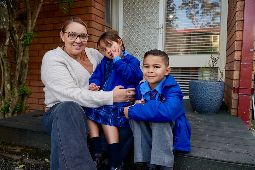 A mum sits with her two kids in school uniform 