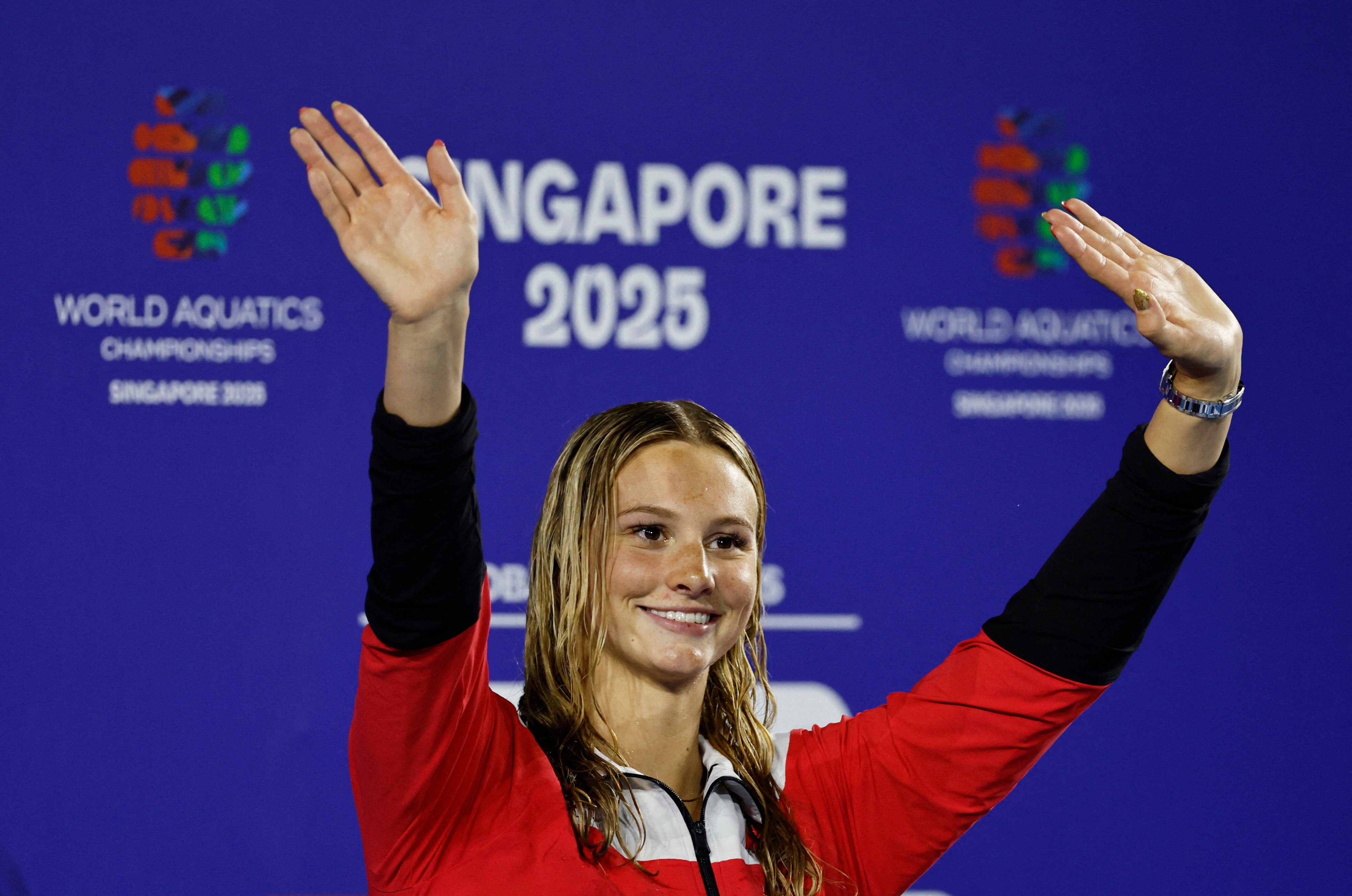 A young woman on a medal podium holding her hands up and smiling.