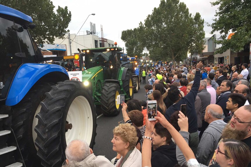 Crowds watch as a line of tractors move through the street in protest against a new youth detention facility.