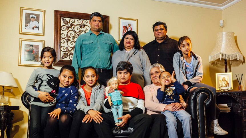 An extended Indian family, including children and adults, poses for a photo in thier living room.