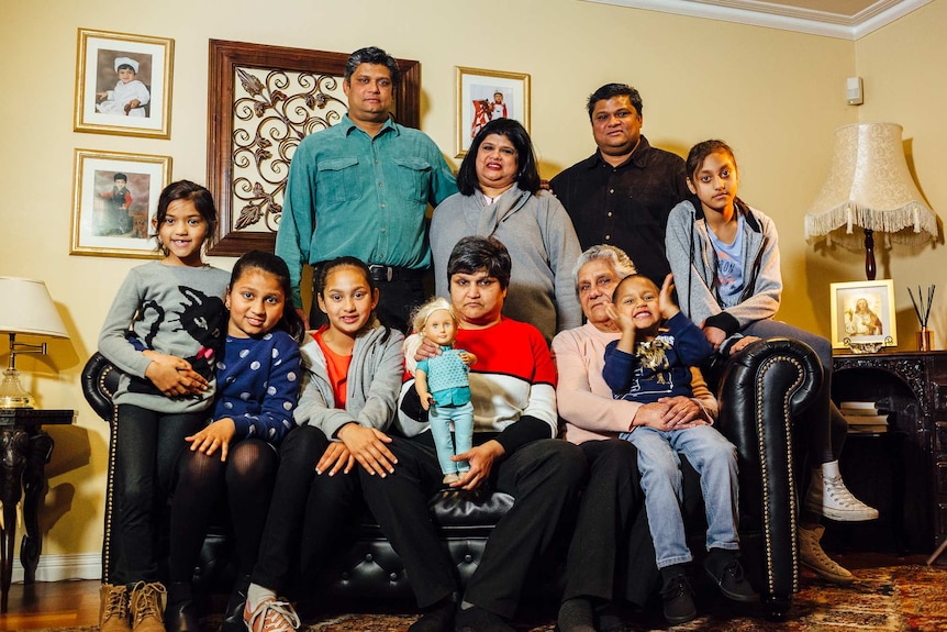 An extended Indian family, including children and adults, poses for a photo in thier living room.