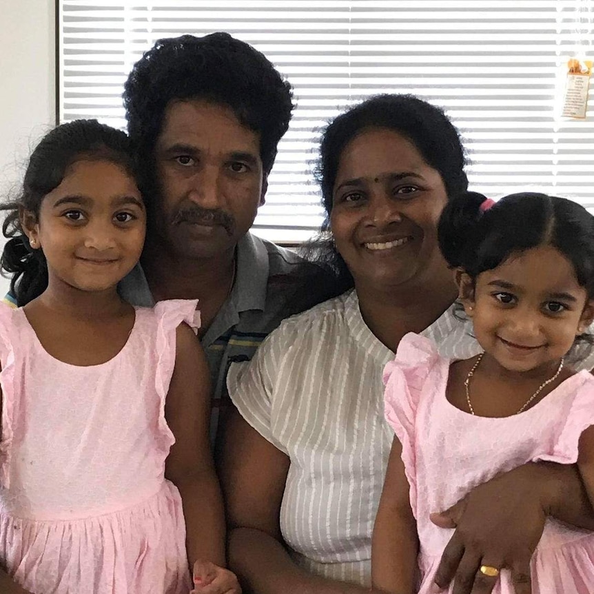 Nades and Priya Murugappan sit with daughters Kopika and Tharnicaa on their laps. Priya smiles while husband Nades is serious.