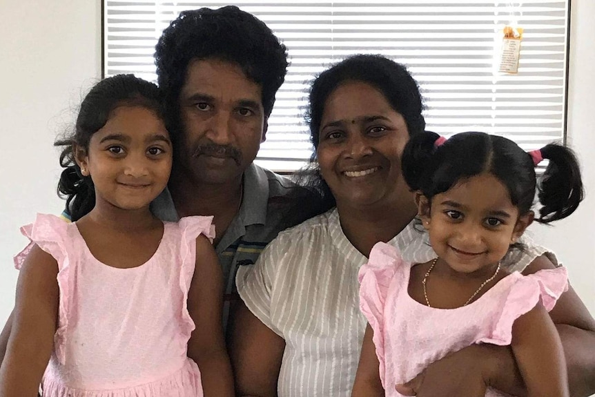 Nades and Priya Murugappan sit with daughters Kopika and Tharnicaa on their laps. Priya smiles while husband Nades is serious.