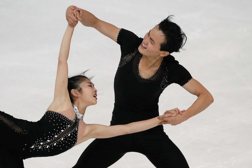 Male figure skater smiles as he spins his female partner.