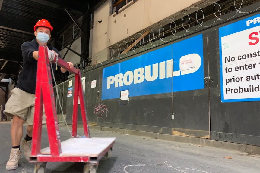 A worker pushes a trolley on a Probuild site in A'Beckett St, Melbourne with branding in background.