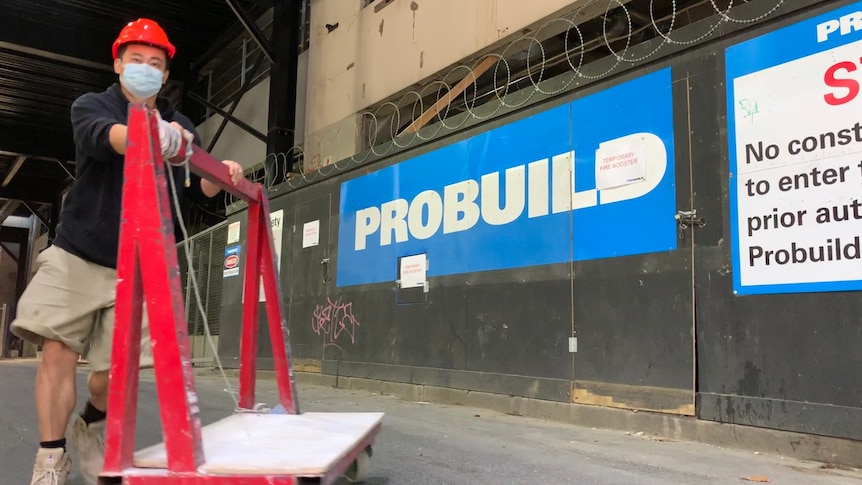 A worker pushes a trolley on a Probuild site in A'Beckett St, Melbourne with branding in background.