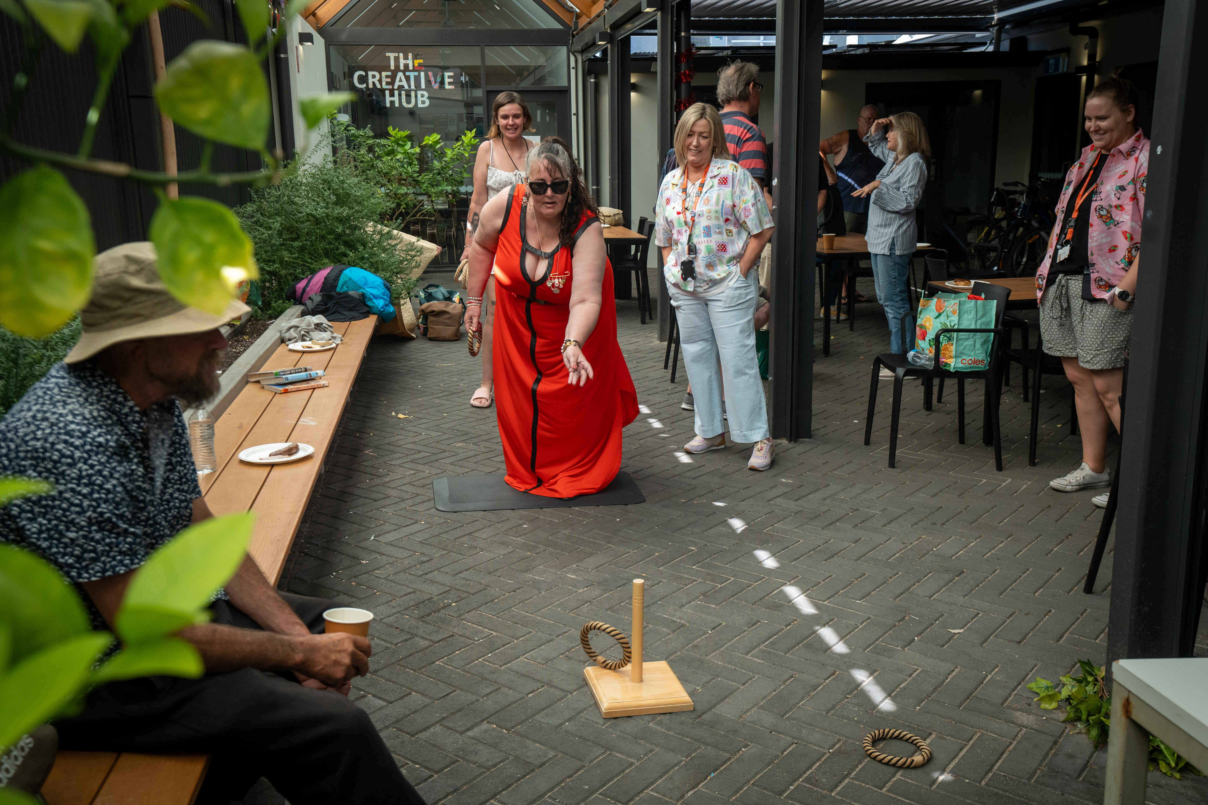 woman in red dress plays game tossing wooden ring as people observe