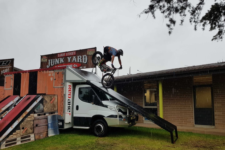 A bike rider goes down a ramp attached to a truck in front of a building.