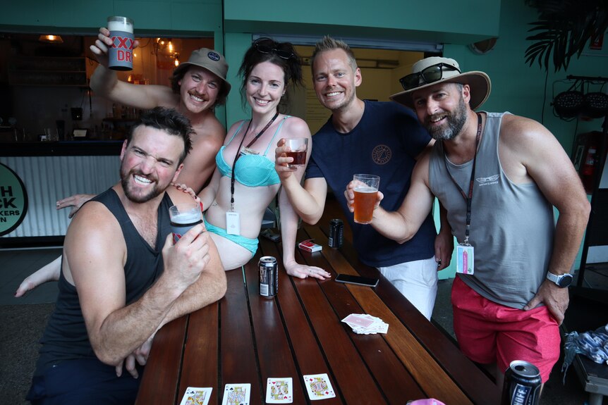 Four men and a woman are smiling as the hold up their beers.