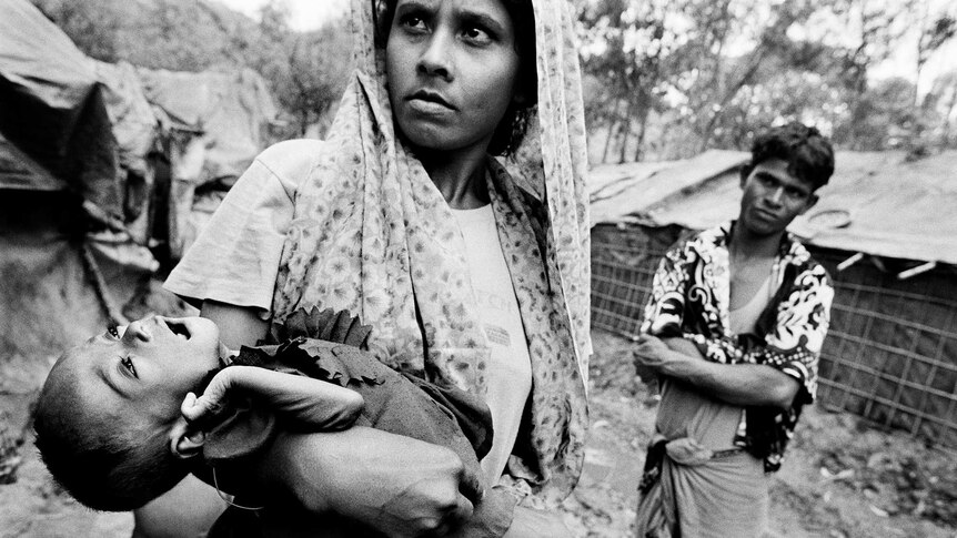 A Rohingya mother looks into the distance as she cradles her sick child.