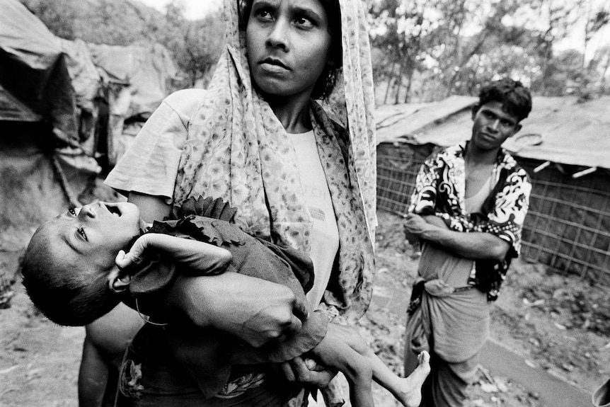 A Rohingya mother looks into the distance as she cradles her sick child.