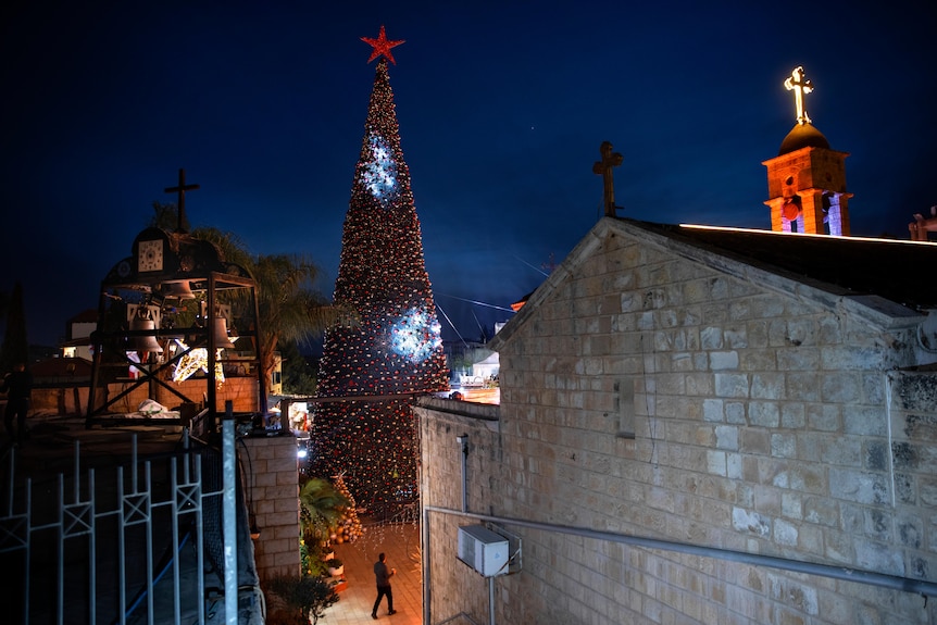 A man walks by a Christmas tree during the lighting ceremony, outside the Greek Orthodox Church of the Annunciation