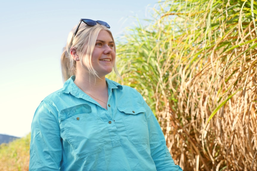 a woman smiles into the distance next to a cane field 