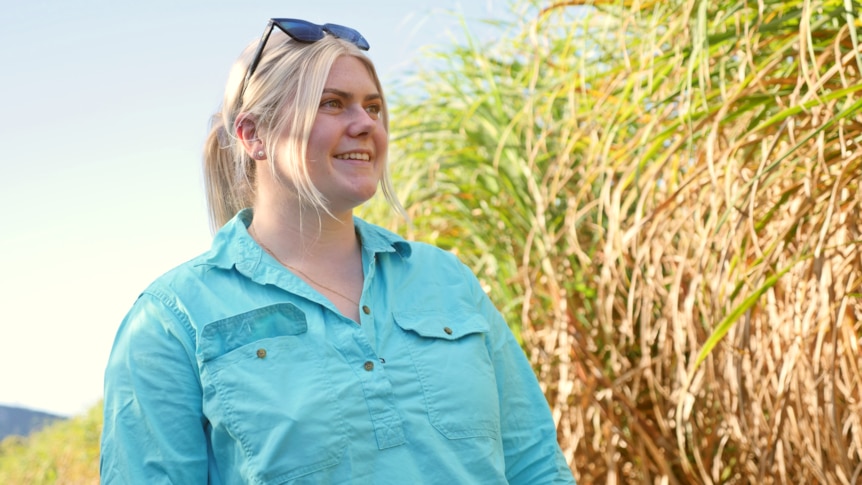 a woman smiles into the distance next to a cane field 