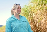 a woman smiles into the distance next to a cane field 