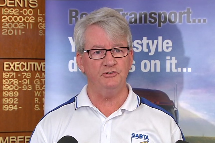 A man speaking in front of banners displaying SA Road Transport Association