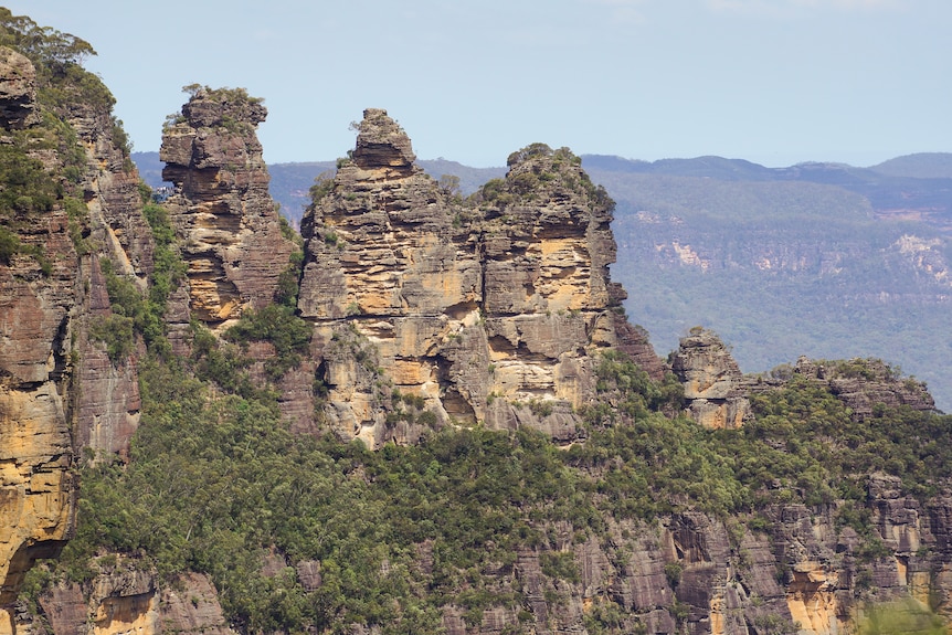 The Three Sister Rock formations standing freely. Below are some green brushes covering the bottom with cliff faces behind it
