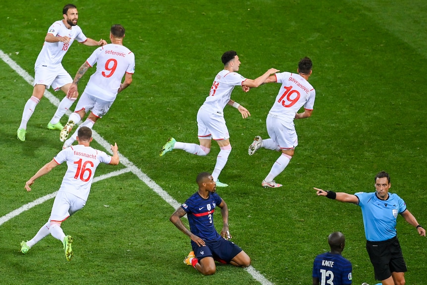 Los jugadores de Suiza salen corriendo mientras los jugadores franceses se arrodillan en el suelo