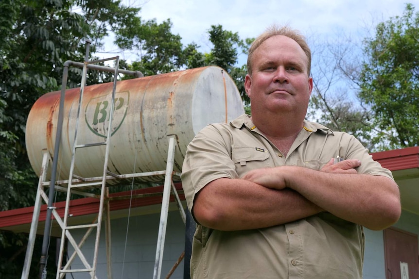 A man standing with his arms folded in front of an old tank with BP written on it.