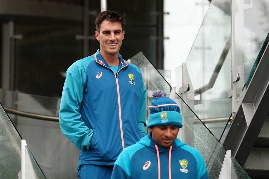 Pat Cummins smiles while walking out of the Australian dressing room with Usman Khawaja