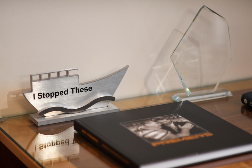 A small trophy of a boat, engraved with the words 'I stopped these', sits on a wood table.