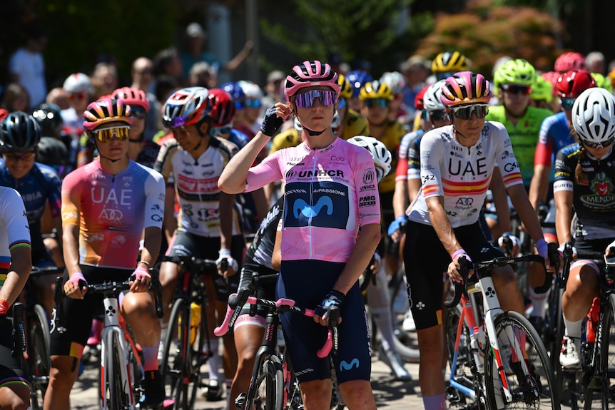 Annemiek van Vleuten touches her ear standing in front of a lot of women cyclists