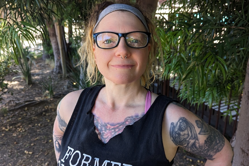 Stephanie Kemmerer, smiling widely, wears singlet with words: Former conspiracy theorist. She has curly fair hair and tattooes.