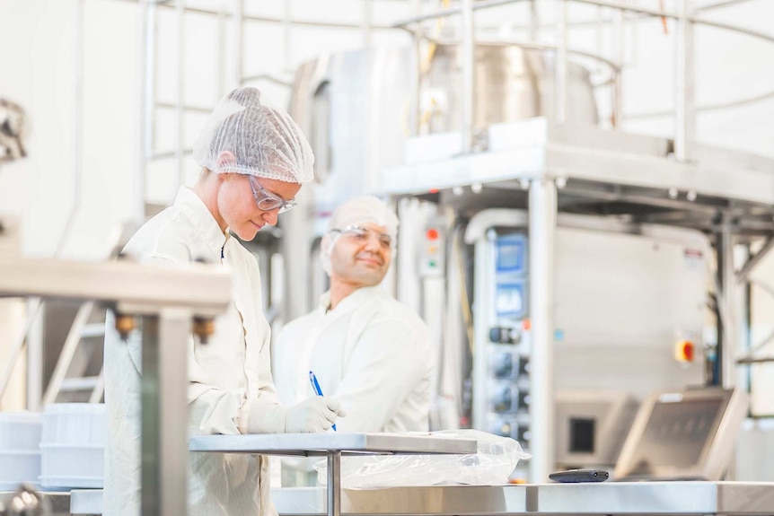 two people in white protective equipment stand in a laboratory