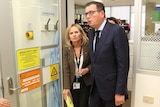 Daniel Andrews and Sharon Lewin walk through a door in a medical facility.