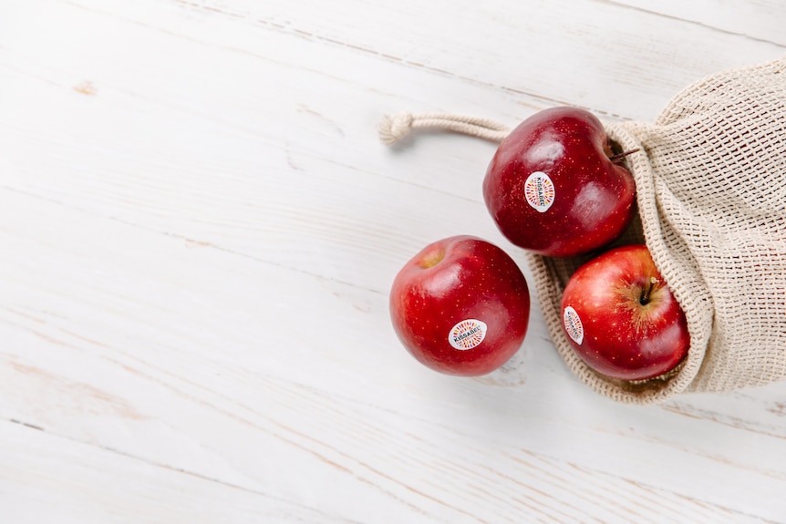 Apples in a reusable produce bag sitting on a bench.