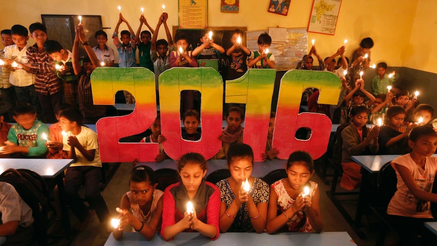 School students sit around large 2016 numerals and hold candles as they pray in a classroom.
