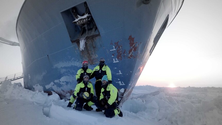 Expedition members standing on ice next to ship