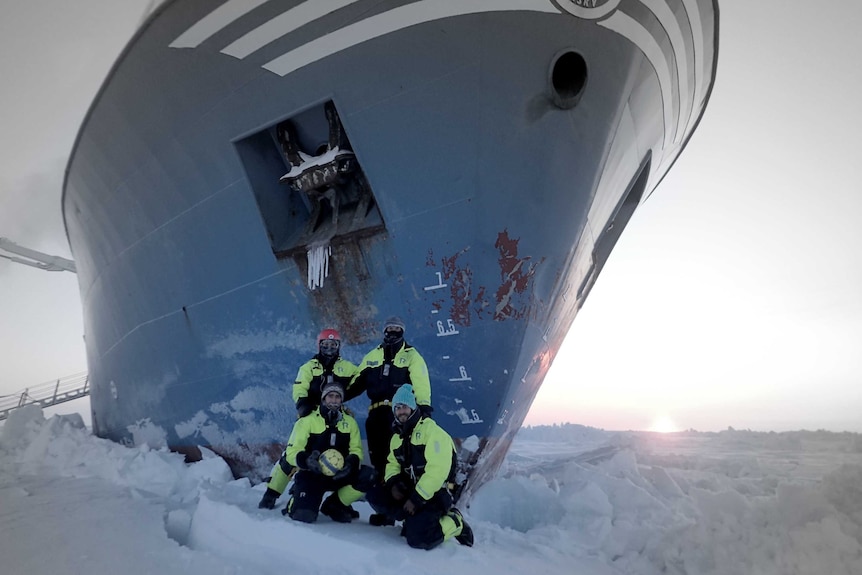 Expedition members standing on ice next to ship