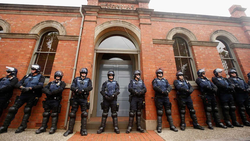 Victoria Police offices stand in front of a building wearing vests, glasses and helmets.