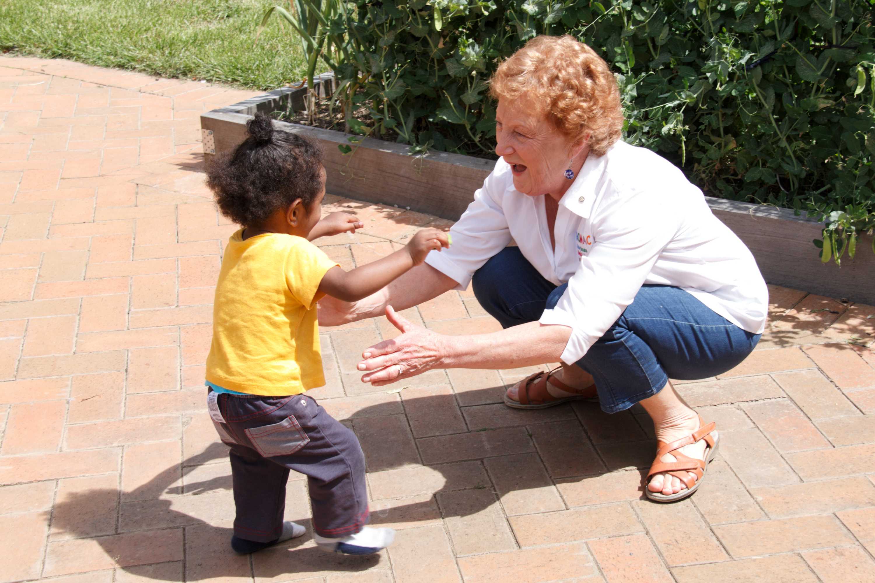 A woman holds her arms out to embrace a toddler.