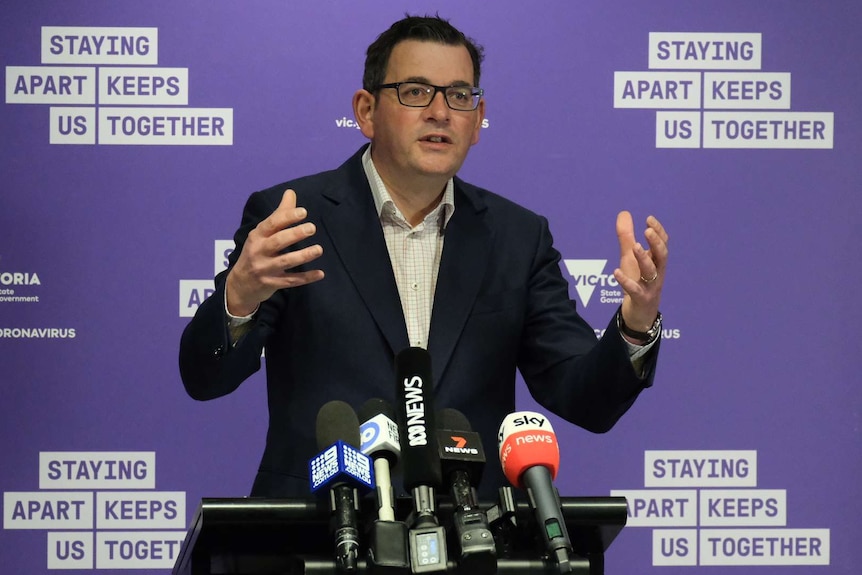 Premier Daniel Andrews addresses press conference with a purple back drop and microphones in front of him.
