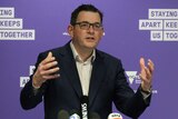 Premier Daniel Andrews addresses press conference with a purple back drop and microphones in front of him.
