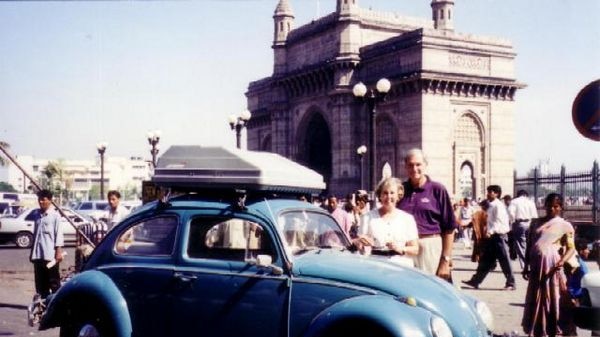Two people stand behind their VW Beetle in a street in India.