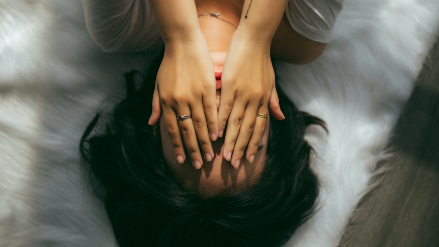 A young person lies down, their hands over their face.