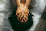 A young person lies down, their hands over their face.